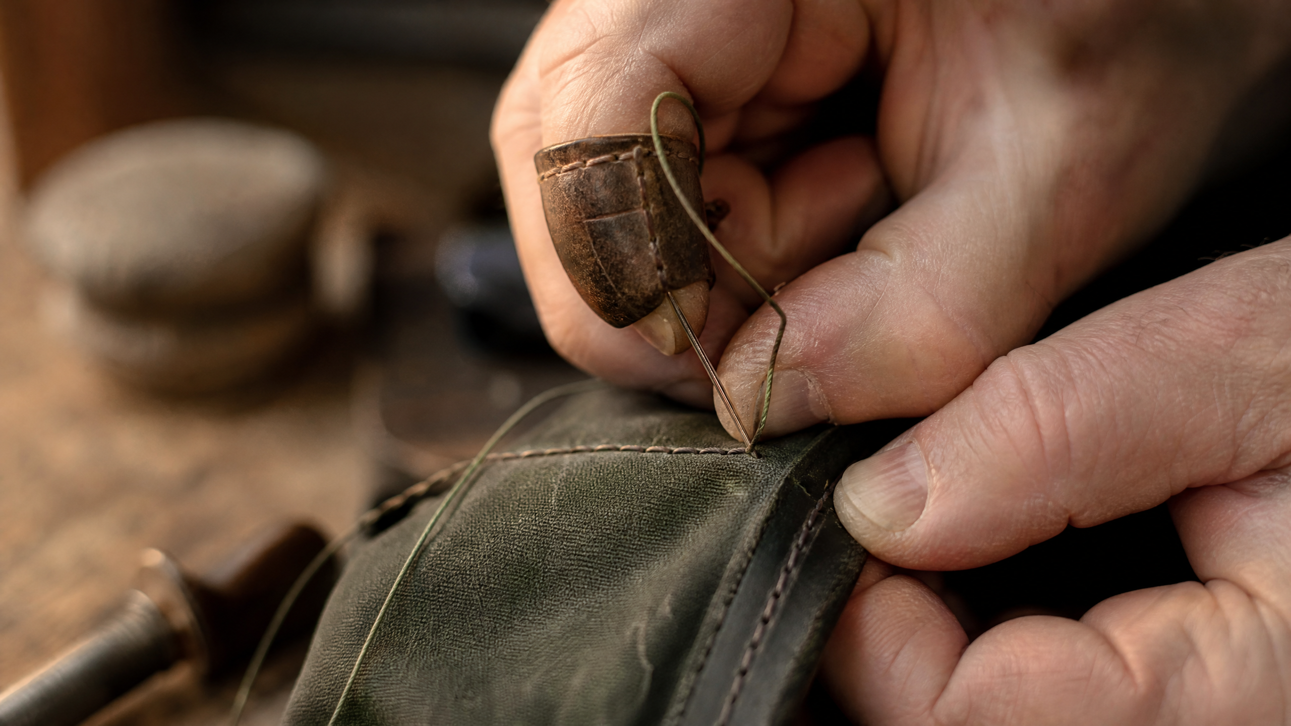Artisan craftsman hand-stitching a waxed canvas golf bag in a workshop