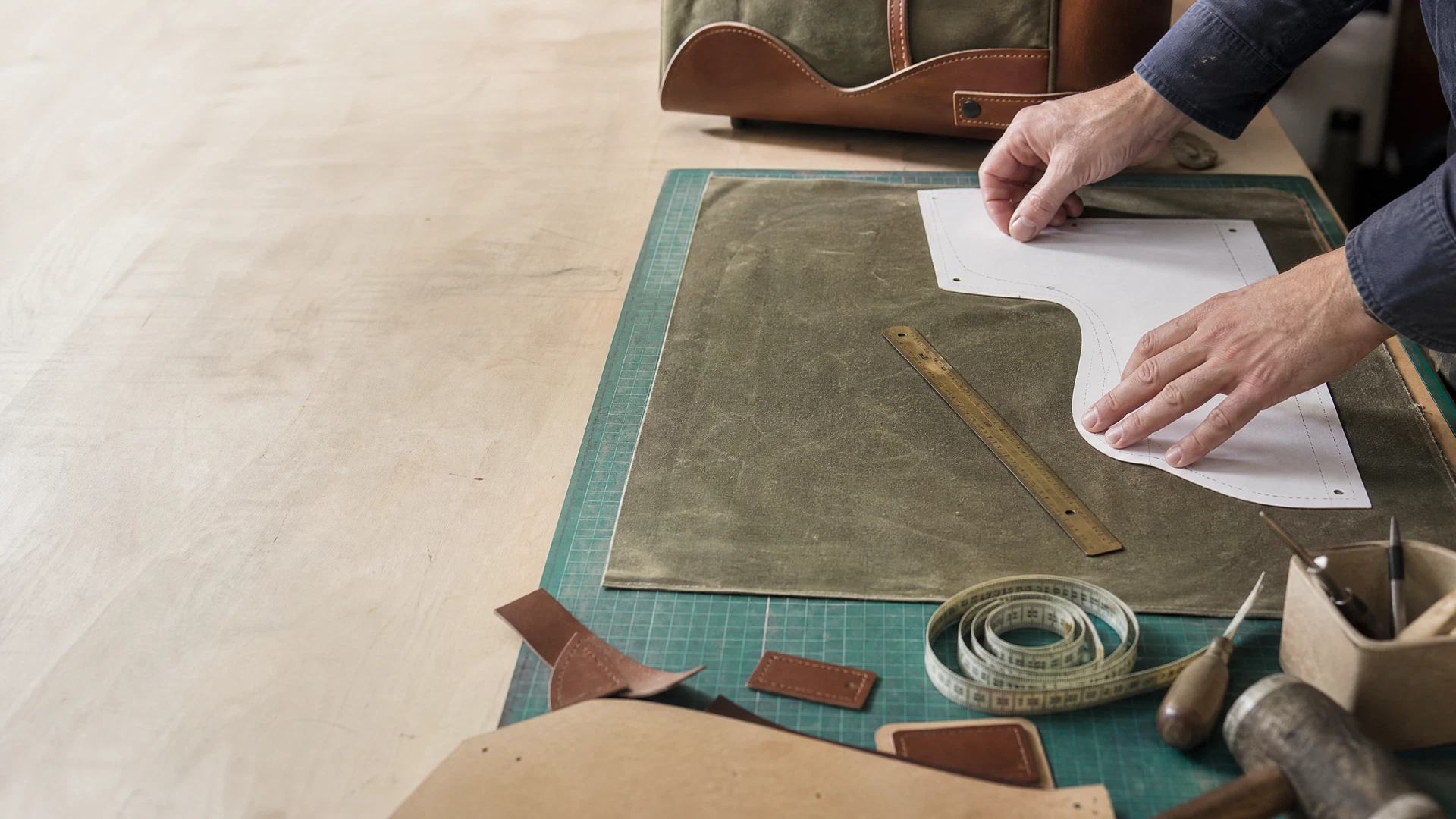 Close-up of a craftsman working on a waxed canvas golf bag, highlighting the precision stitching and leather trim details.