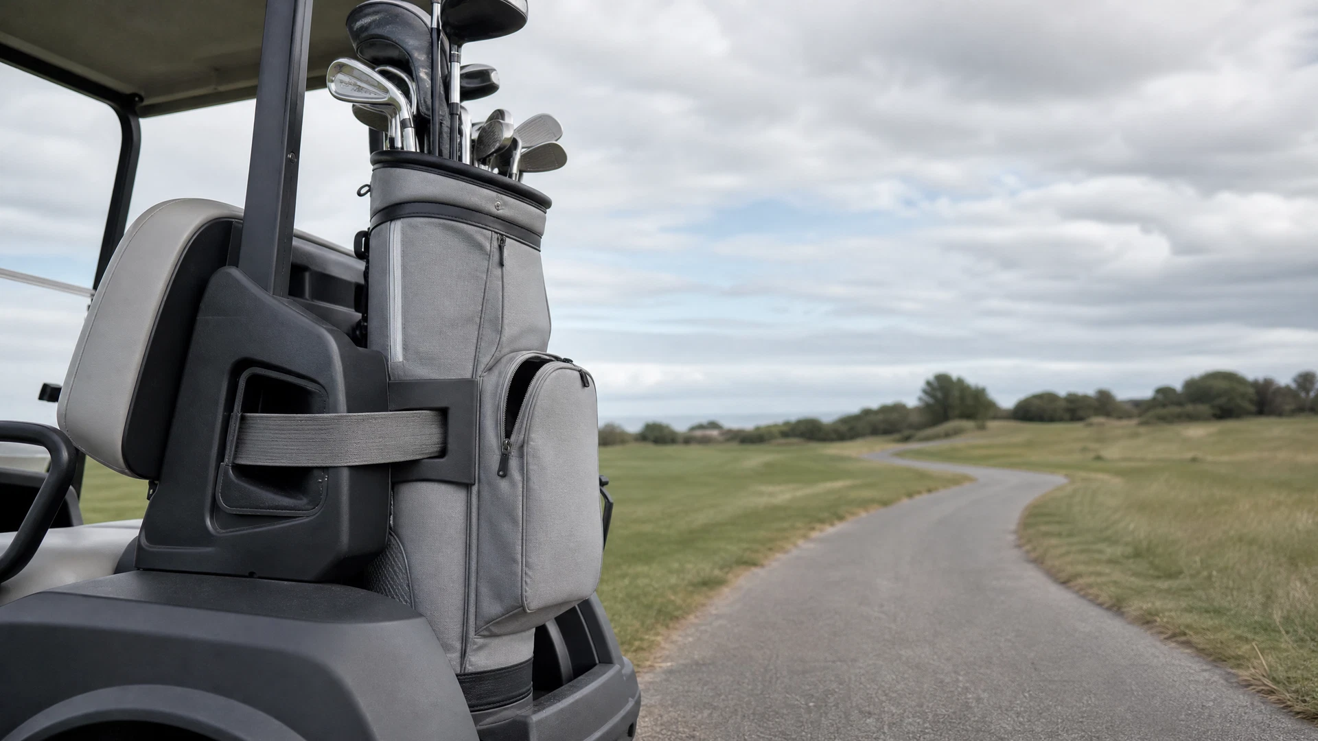 Stone-gray golf cart bag mounted on a cart, showing a strap routed through its pocket-access channel.