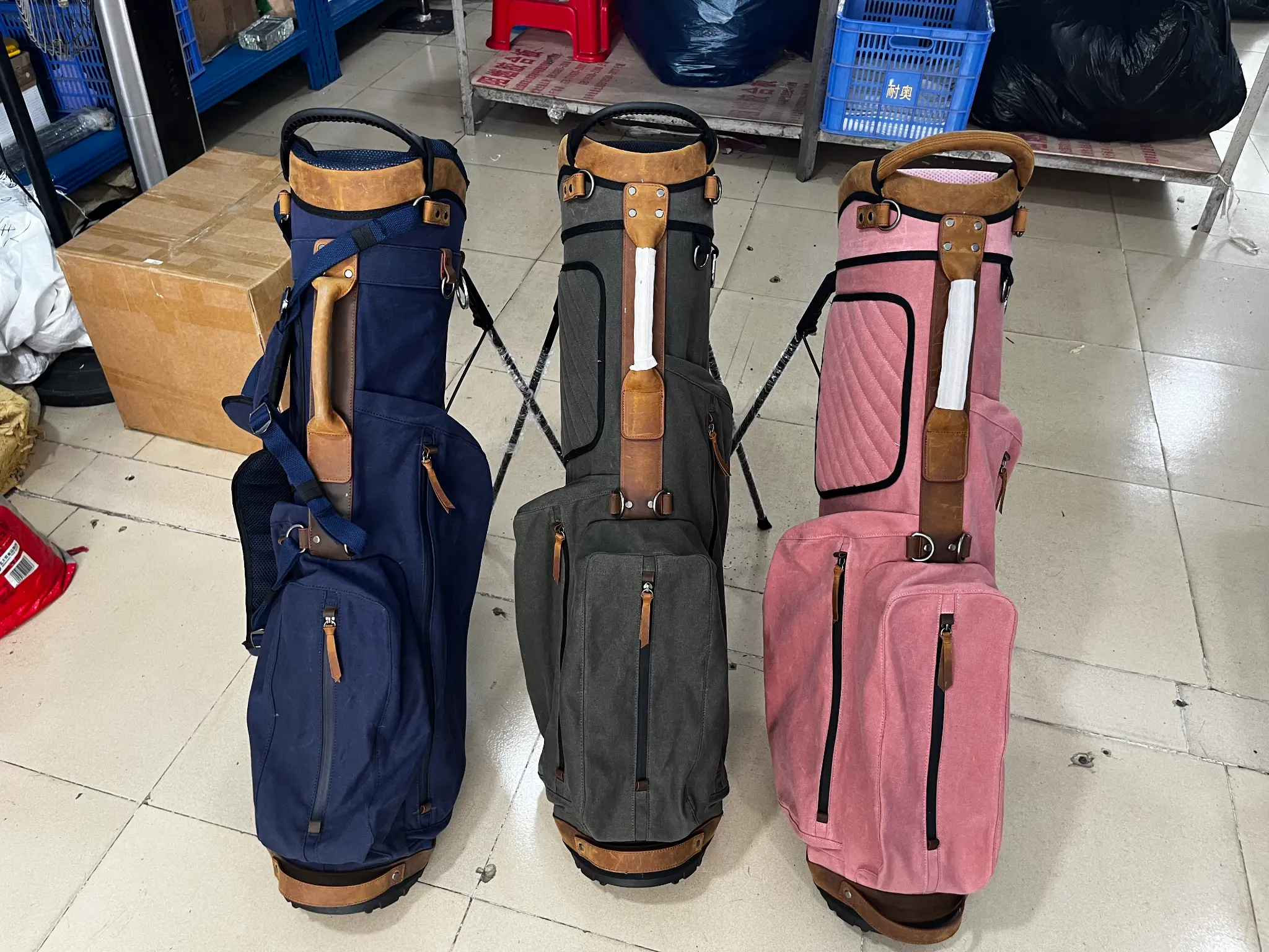 Three custom waxed canvas and leather-trim golf stand bag samples in a workshop.